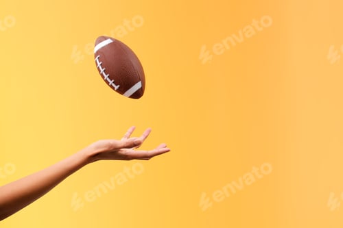 Preview: Hand Throwing Up And Catching American Football Isolated On Yellow Background