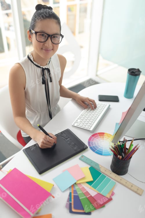 Preview: High angle view of Asian female graphic designer using graphic tablet at desk in a modern office