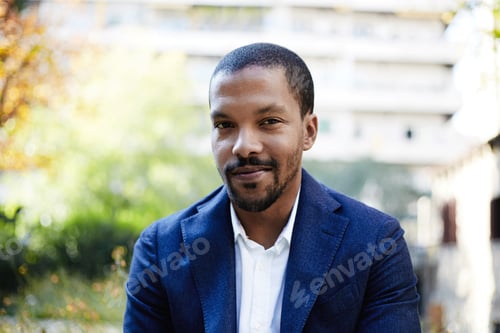 Preview: Portrait of Happy confident young African-American businessman in formal wear sitting at city park.
