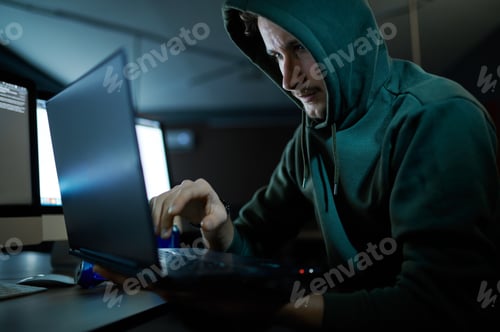 Preview: Male internet hacker in hood works on laptop