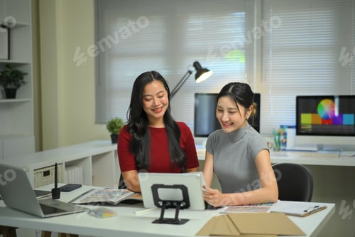 Preview: Young women discussing graphic design work at office desk, creative teamwork