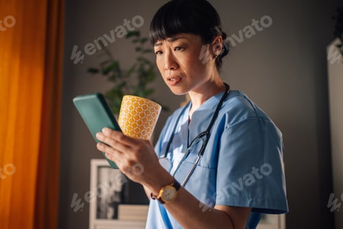 Preview: Asian nurse surprised by message on phone drinking morning tea