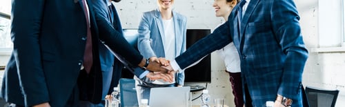 Preview: panoramic shot of cheerful businesswomen and multicultural men putting hands together