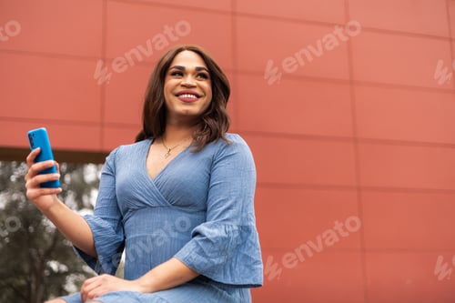 Preview: Trans woman in blue dress using cellphone over a red background