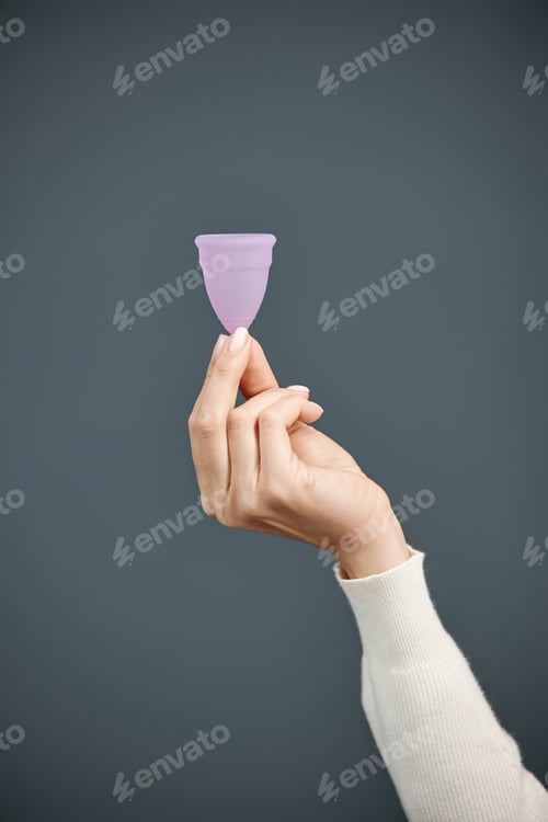 Preview: Hand Holding Pink Menstrual Cup on Blue