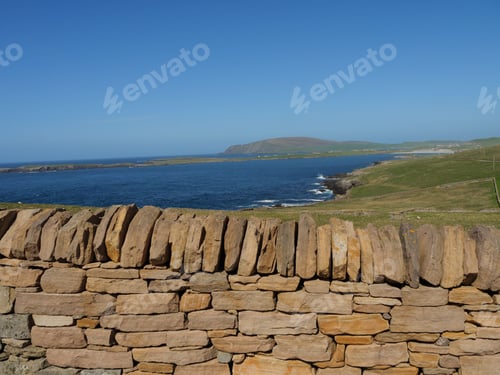 Preview: Scenic landscape of a stone wall in the foreground with a mountain and body of water