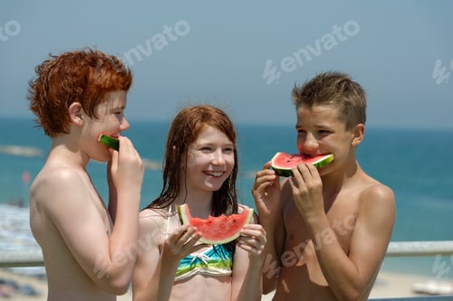 Preview: Italy, girl and two teenage boys eating watermelon slices at the beach