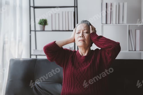 Preview: Senior woman sitting in the living room at home and showing body aches, aging sickness, body aches o