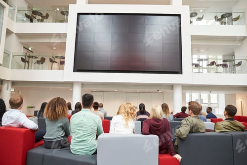 Preview: Students watching big screen in university atrium, back view