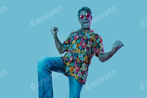 Preview: Senior man posing in studio under colored gel lights.