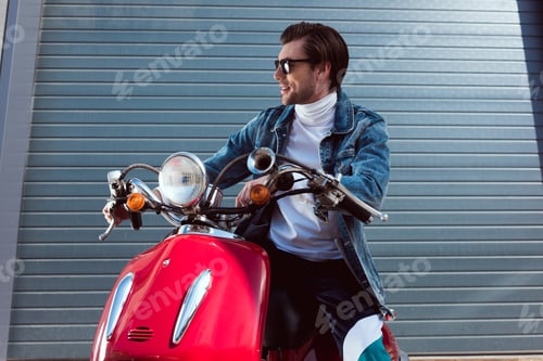 Preview: stylish young man in denim jacket on vintage red scooter looking away