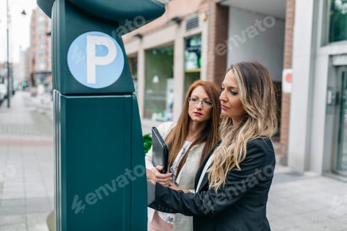 Preview: Two businesswomen at pay and display ticket machine in the city