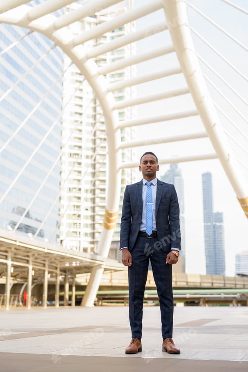 Preview: Full body shot of young handsome African businessman wearing suit in the city outdoors