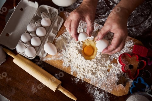Hands Cracking Eggs into Flour on a Wooden Board