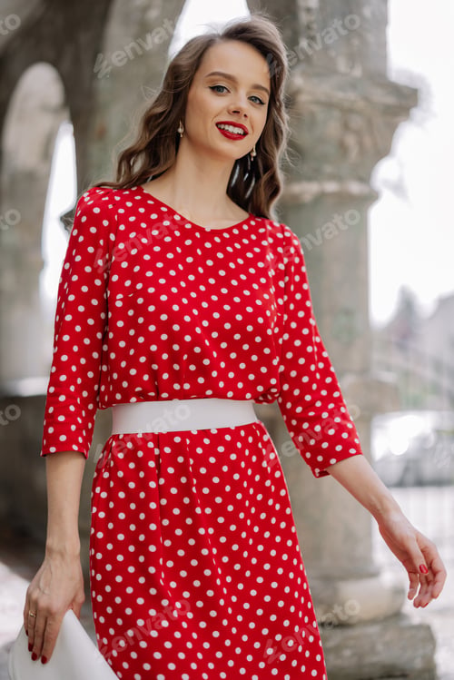Preview: Smiling woman wearing red polka dot dress standing in urban setting
