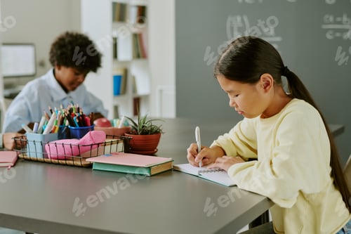Preview: Asian Girl Writing in Notebook While Black Boy Studying in Classroom
