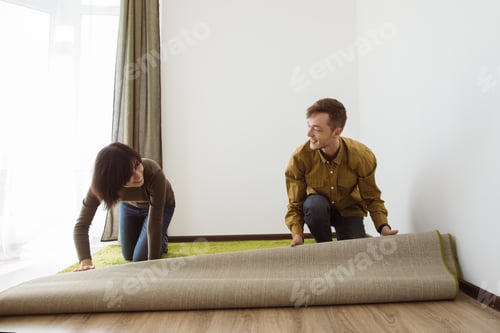 Preview: Young couple unrolling carpet in new apartment
