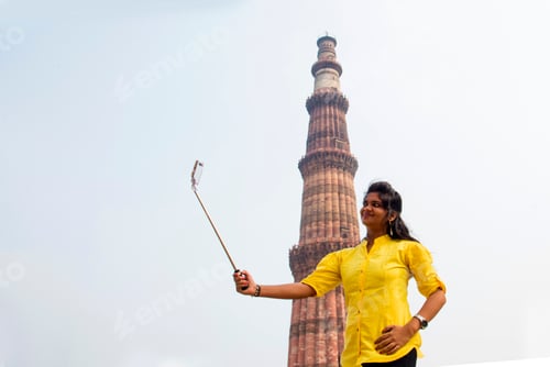 Preview: Tourist woman taking selfie in front of Qutub Minar, Delhi, India.