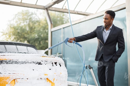 Preview: Portrait of handsome bearded young African businessman washing his yellow car with foam