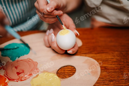Preview: Women painting easter eggs on wooden table with palette and brushes