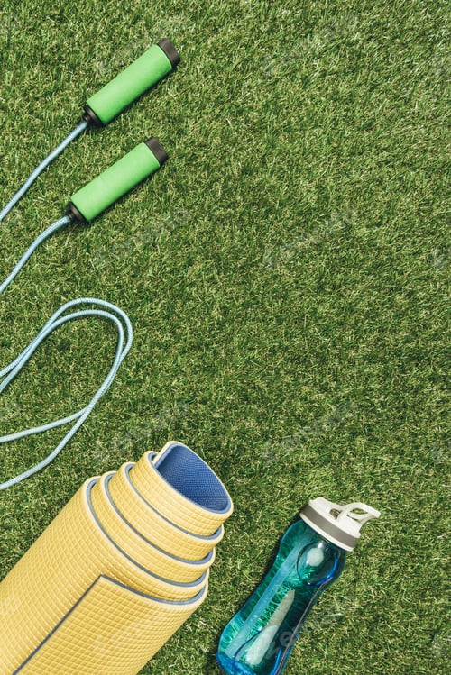 Preview: top view of arranged yellow mat, skipping rope and water bottle on green grass