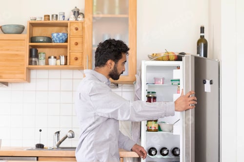 Preview: A man is opening a refrigerator full of various food items in a well-lit, modern kitchen.