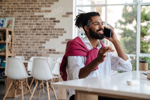 Preview: Smiling african american guy talking on cellphone and working in office
