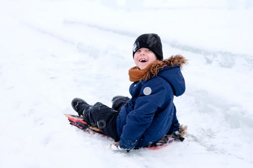 Preview: happy boy slides down the hill on the ice. Winter fun outdoors. Winter games in the snow.