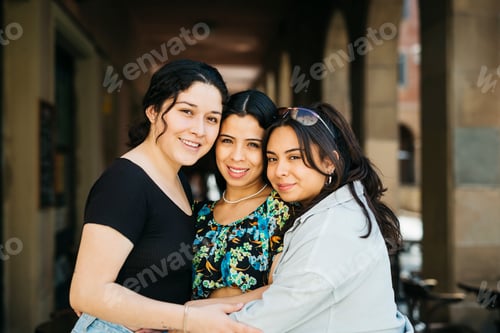 Preview: Three smiling young women embracing under city archway