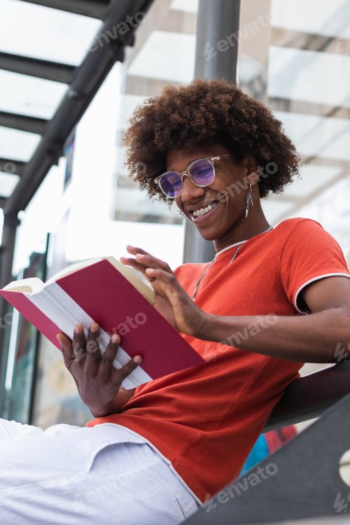 Preview: Happy relaxed young African American guy reading book while waiting for bus