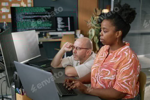 Preview: Young Adult Black Woman Collaborating with Middle Aged Caucasian Man Coding