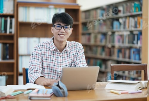 Preview: Young Asian male sitting inside a library alone doing research.