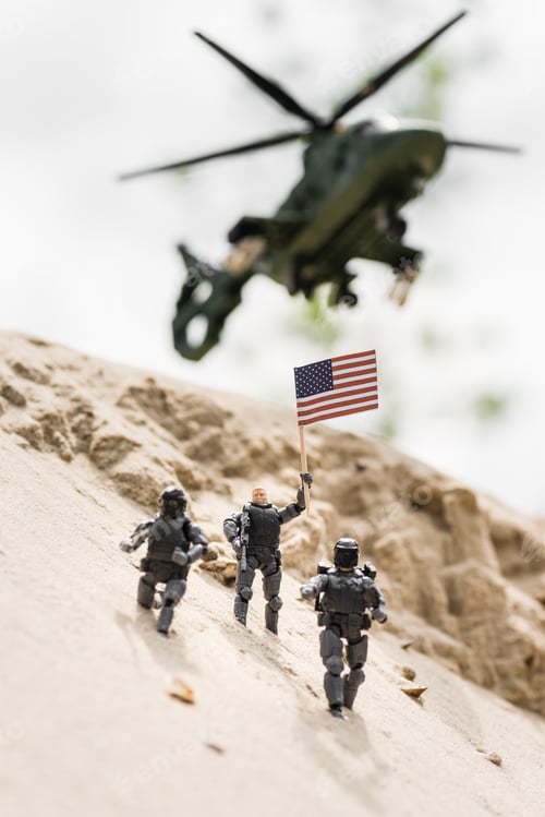 Vista previa: selective focus of toy soldier with weapon holding american flag on sand with helicopter on