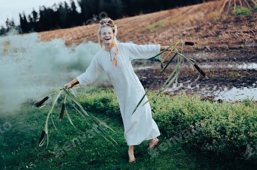 Preview: Happy woman in white dress with smoke bomb and reeds dancing on muddy field