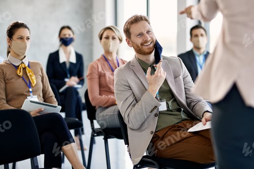 Preview: Happy businessman taking off his face mask while answering question during education event.