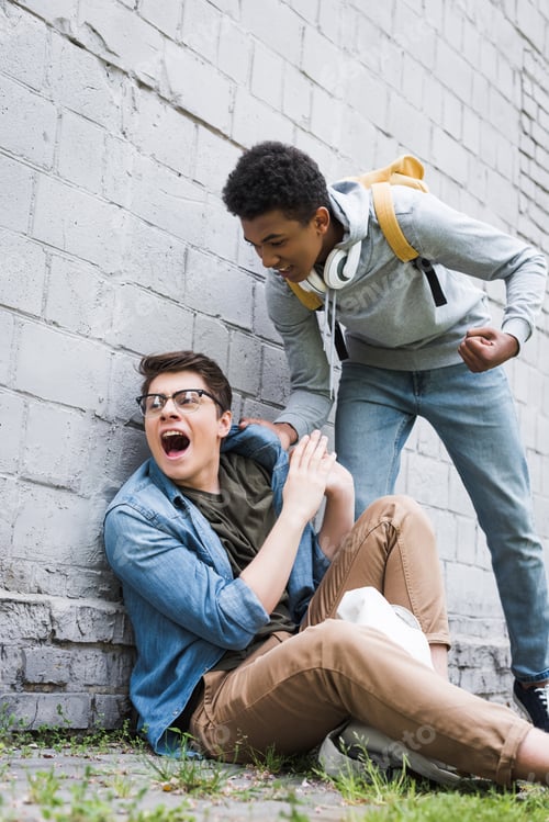 Preview: aggressive and brunette african american boy going to punch frightened boy in glasses