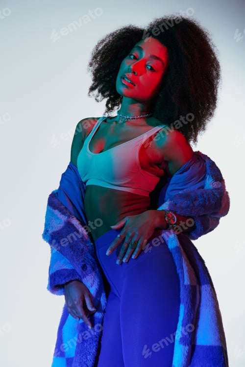Preview: appealing sexy african american woman in fashionable stylish faux fur looking at camera in lights