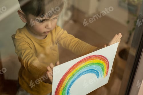 Preview: Little kid holding a drawing of a rainbow through the window