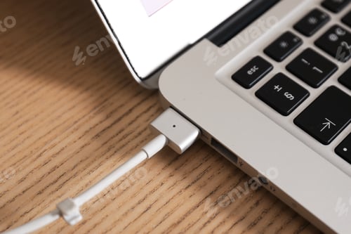 Preview: Charge cable connected to laptop on wooden table, closeup