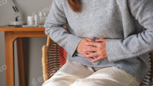 Preview: A sick woman suffering from stomachache, abdominal pain while sitting on sofa at home