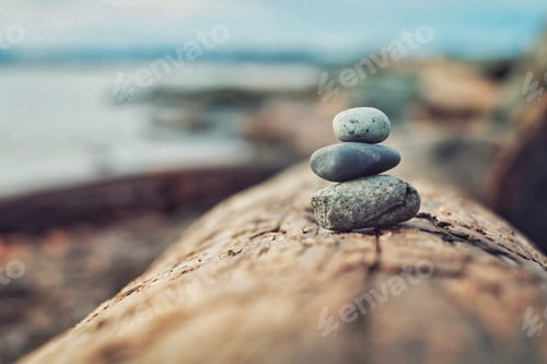 Preview: Three round rocks stacked on a log on the beach