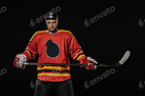 Preview: professional ice hockey player holding hockey stick and looking at camera isolated on black