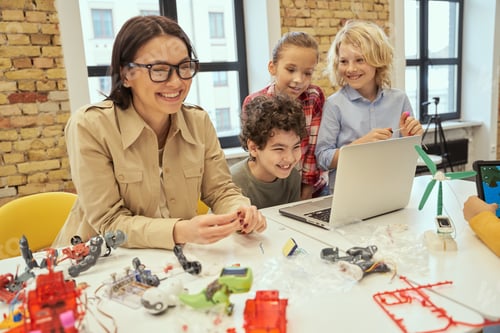 Preview: Joyful kids laughing together with their young female teacher while learning how to assemble robot