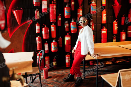 Preview: African woman posed against wall with old extinguisher.