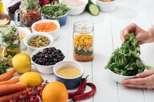 Preview: cropped view of woman taking greenery from bowl on wooden white table