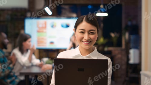 Preview: Asian employee working on laptop, looking at camera, smiling