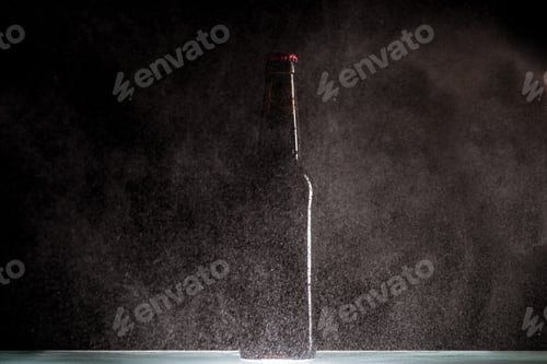Preview: selective focus of beer bottle with spraying water around at surface on black background