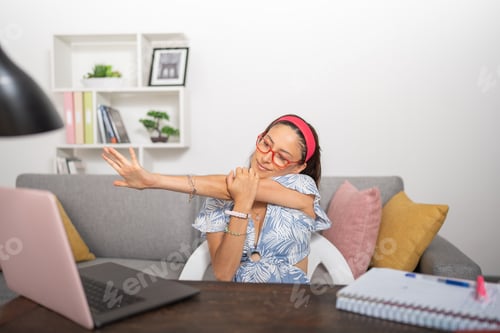 Preview: Young female student stretching her arms, sitting behind her desk.