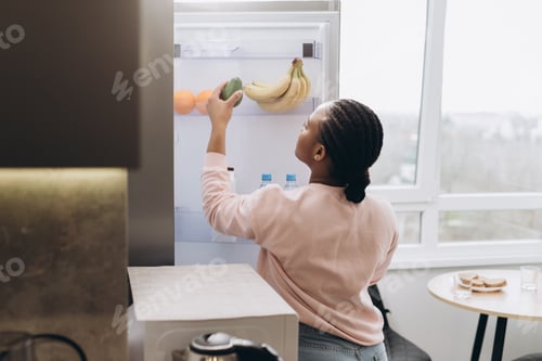 Preview: Woman taking avocado from refrigerator in modern kitchen
