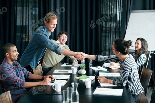 Preview: Shot of two colleagues shaking hands in a boardroom while coworkers look on